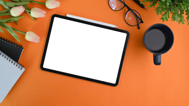 istock Digital tablet with blank screen, coffee cup ,glasses and notebook orange background. 1316560259