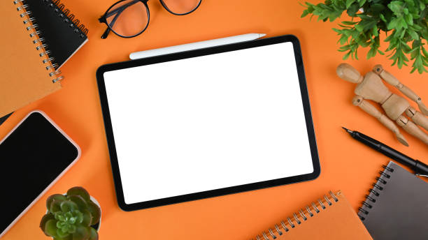 istock Digital tablet with blank screen, smart phone, house plant ,glasses and notebook orange background. 1316560321