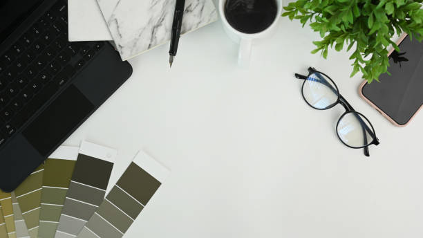 istock Graphic designer workspace with notebook, glasses, houseplant, smart phone keyboard and color swatches on white table. 1316560367