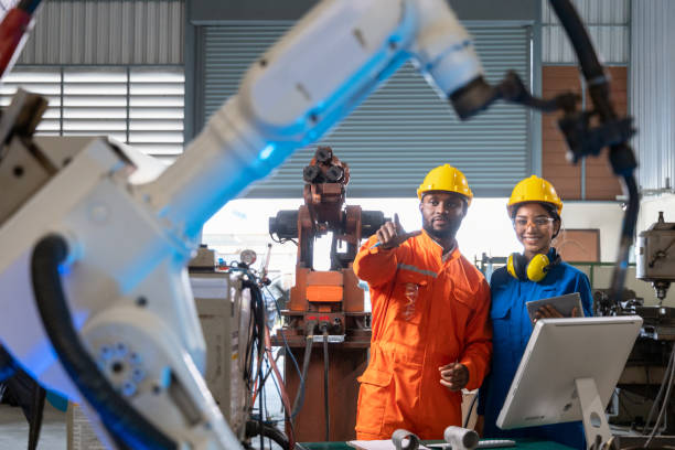 istock African male engineer standing pointing robotic arm and female engineer standing smiling and holding tablet in factory. 1316561129