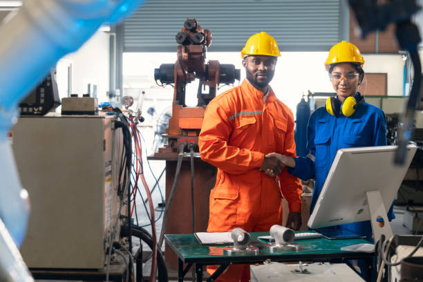 istock African male engineer and asian female engineer looking at camera smiling  and shakehands together in side of robotic arm. 1316561133