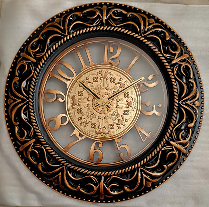 A very Royal Golden brown and black Colored wall clock with some very interesting design, lying on a white sheet