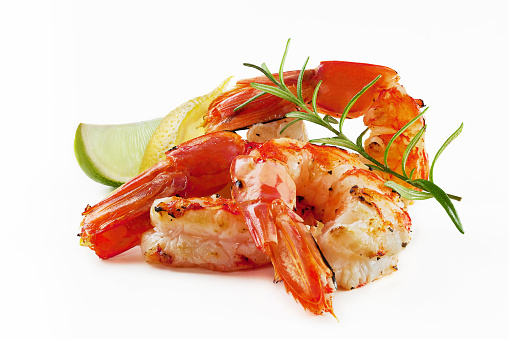 Closeup of shelled and grilled prawn tails with wedges of fresh lemon, lime and sprig of aromatic rosemary on white background. Delicious seafood appetizer