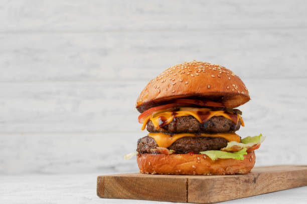 istock Double cheeseburger served on wooden board against white blurred background 1316568111