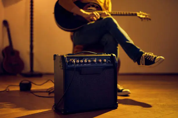 Male musician playing acoustic guitar on the amplifier in retro vintage room.