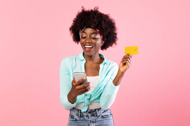 istock Happy African Lady Using Smartphone Holding Credit Card, Pink Background 1316568284