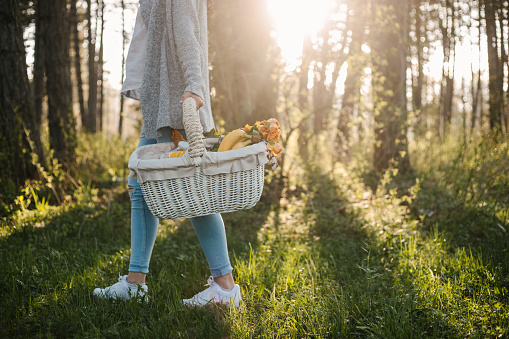 Woman in blue jeans casually dressed holding a white picnic basket with flowers, food and drink