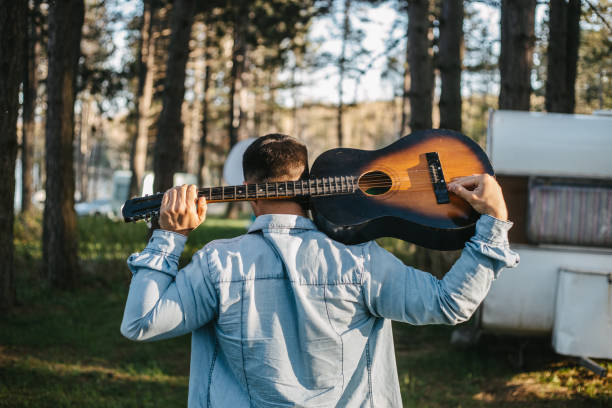A young man holding a guitar in the forest ready to play