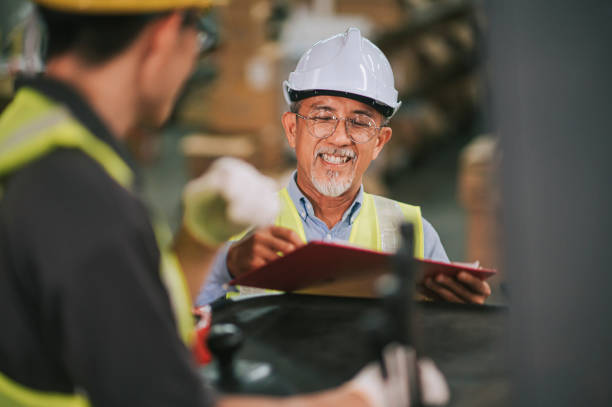 responsabile supervisore magazzino cinese asiatico firma documenti che ricevono merci dal suo operaio collega che opera carrello elevatore che lavora in fabbrica industriale - factory manager manual worker foreman foto e immagini stock