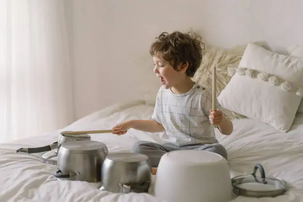 Cute young boy using wooden sticks to bang saucepans that are set up like a drumset. Quarantine time