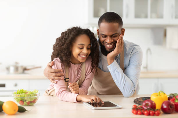 istock Black man and girl cooking in kitchen using digital tablet 1316572263