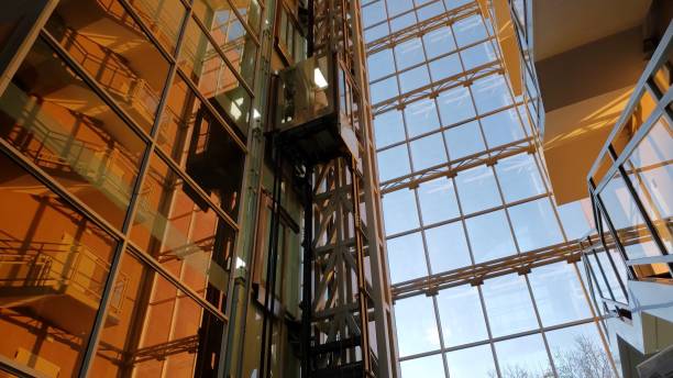 Corporate building window wall with abstract geometric reflections and golden hour sunlight. Modern glass elevator rises up. Mirrored walls of business skyscraper. Odessa, Ukraine, 02 22 2021
