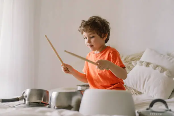 Cute young boy using wooden sticks to bang saucepans that are set up like a drumset. Quarantine time