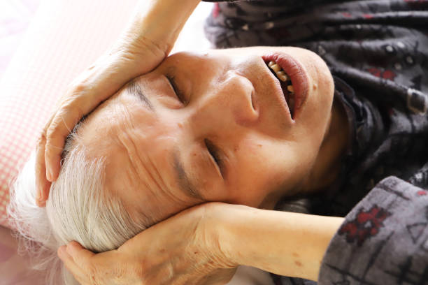 Senior Lady lying On The Nursing Bed With closing eyes and both hands on her head suffering