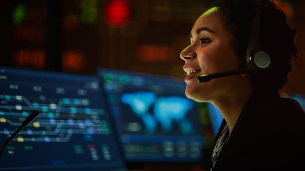 istock Close Up Portrait of Multiethnic Female IT Technical Support Specialist Talking with a Client in Headphones and Working on Desktop Computer in Monitoring Control Room with Big Digital Screens. 1316574087