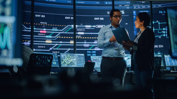 istock In the System Control Room Project Manager and IT Technical Engineer with Laptop Have Discussion, surrounded by Multiple Monitors with Graphics. Big Monitor Shows Interactive Server Blockchain Info. 1316574119