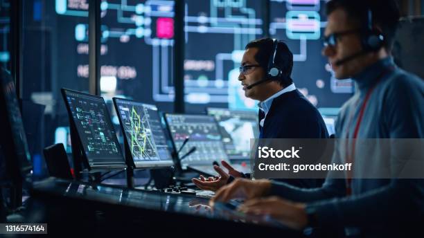 Portrait Of Professional It Technical Support Specialist Working On Computer In Monitoring Control Room With Digital Screens Employee Wears Headphones With Mic And Talking On A Call Stock Photo - Download Image Now