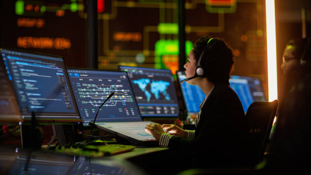istock Multiethnic Female IT Technical Support Specialist Talking with a Client in Headphones and Working on Desktop Computer in Monitoring Control Room with Big Digital Screens with Server Blockchain Data. 1316574165