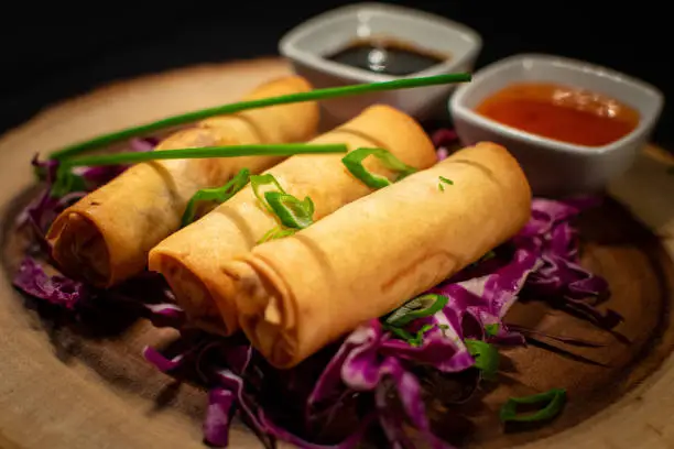 A portion of Chinese style fried spring rolls served with dipping sauces close up
