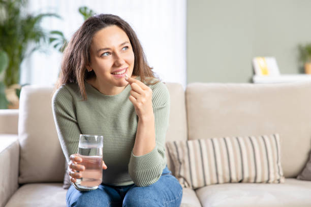 mulher jovem aliviando sintomas da doença tomando uma pílula - capsule pill white nutritional supplement - fotografias e filmes do acervo