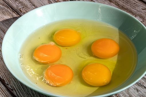 Broken сhicken eggs in bowl of pale turquoise color, 5 pieces, types of scrambled eggs.
Topic: benefits and harms of eating chicken eggs, cholesterol, cooking recipes, healthy natural products.