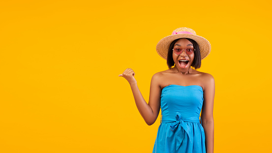 Unbelievable offer. Surprised African American woman with open mouth pointing aside at copy space, orange studio background. Banner design. Summer sale or discount concept