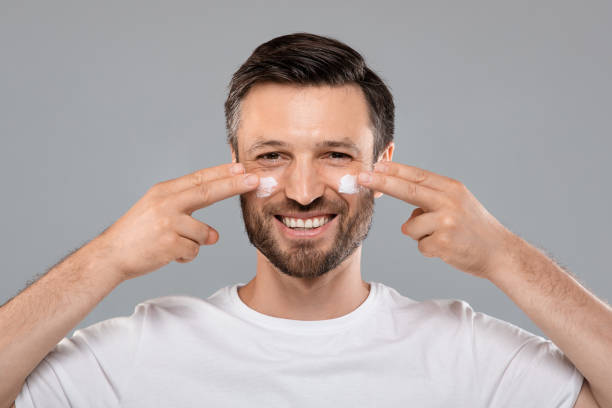 istock Smiling handsome man applying cream on his face, grey background 1316579258