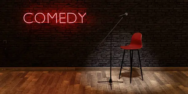 Photo of stage with microphone and stool with red neon lamp with the word COMEDY. space for text