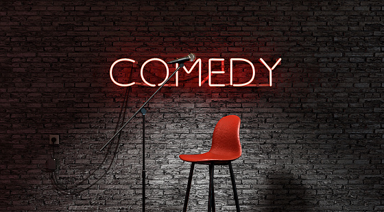stage lit by a spotlight and a red neon lamp with the word COMEDY