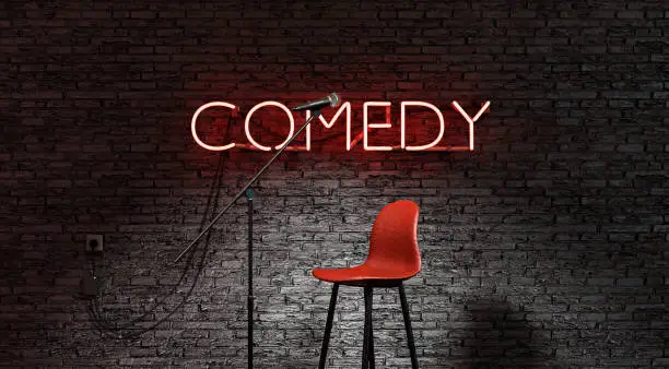 Photo of stage lit by a spotlight and a red neon lamp with the word COMEDY