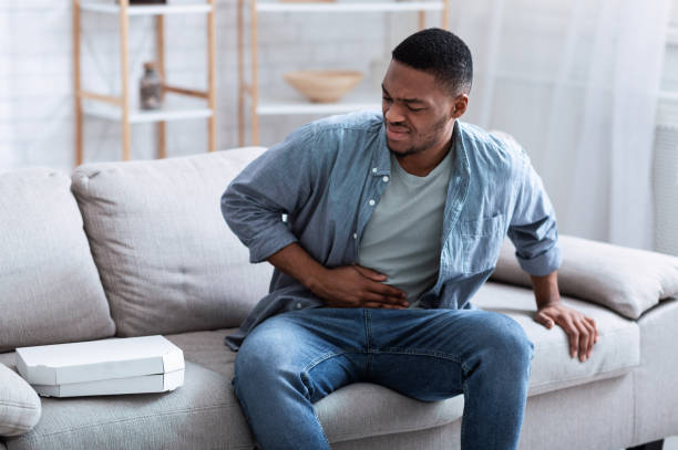 African American Guy Having Stomachache After Eating Pizza At Home African American Guy Having Stomachache After Eating Pizza Touching Aching Stomach Suffering From Pain Sitting On Sofa At Home. Food Poisoning, Gastritis, Abdominal Inflammation And Appendicitis. food poisoning stock pictures, royalty-free photos & images
