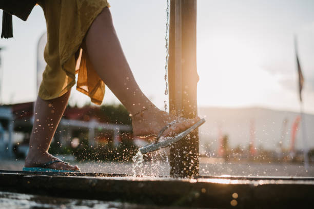 Woman splashing her legs and her slippers using a shower on a beach at sunset. washing sand after beach