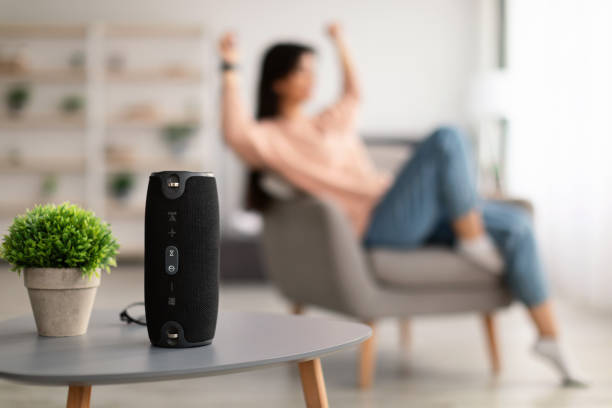 Closeup of smart portable wireless speaker on the table Modern Technology Concept. Closeup of smart portable wireless speaker on the table, selective focus. Young woman listening to music and dancing, sitting on armchair in the blurred background bluetooth stock pictures, royalty-free photos & images