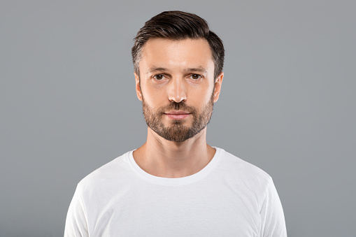 Portrait of handsome bearded man over grey studio background, empty space. Middle-aged bearded man posing for male magazine or blog, youth, healthy lifestyle and male cosmetology concept