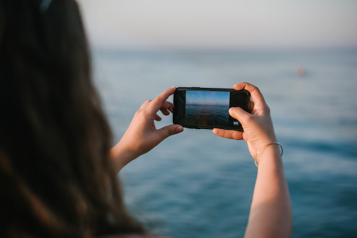 Female hands taking photo of a sea in sunset using smartphone
