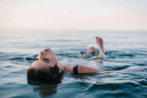 женщина отдыхает на спине в морской воде - sea swimming greece women стоковые фото и изображения