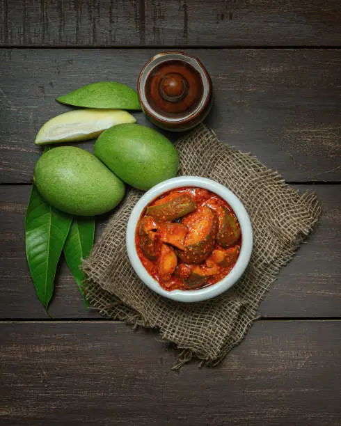 raw mango pickle or aam ka achar or aachar in a white bowl by beautifully styling and on a wooden background theme