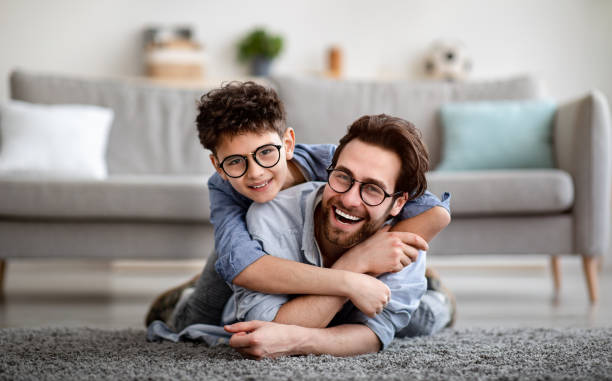 parents and children being friends. joyful father and son having fun, dad lying on floor, carrying boy on back - son imagens e fotografias de stock