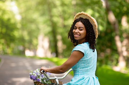 Portrait of lovely black girl in summer dress riding bike at summer park, free space