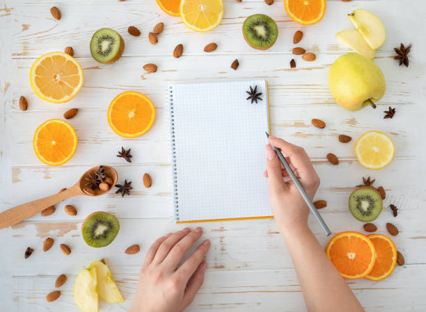 istock Female hand write in empty notebook on healthy food background, top view, flat lay, copy space 1316585981