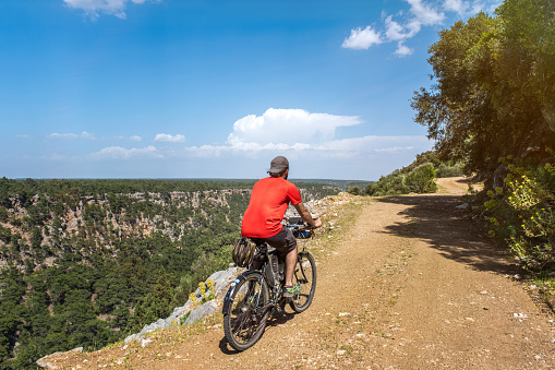 Male cycling athlete, 25-30 years old. Light beard, red shirt. He's riding a bicycle. Open air.Bike helmet mounted.Taken from the background