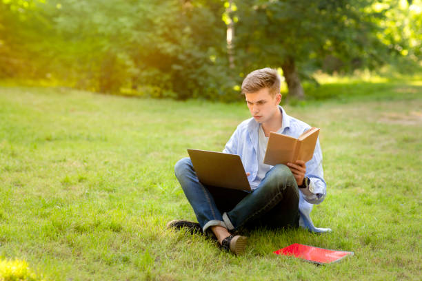 istock Focused Student Guy Doing College Homework With Laptop And Book Outdoors 1316587149
