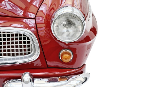 A front view of a red shiny vintage car, isolated on a white background. Part of a shiny red vintage car with headlight and grille, front view.
