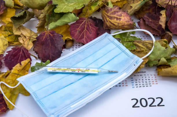 Autumn leaves and thermometer.Seasonal morbidity in the population in 2022. Medical mask and thermometer. stock photo