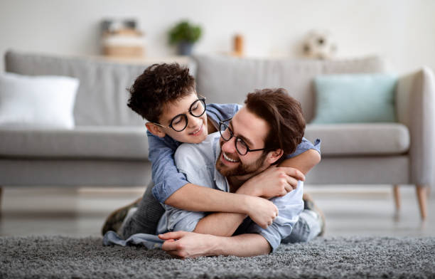 istock Father son bonding. Daddy lying on carpet carrying boy on back and smiling, having fun at home 1316589031