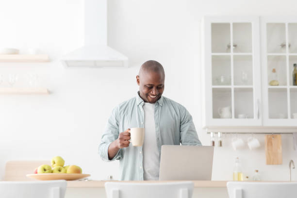 istock Excited mature black man using laptop in kitchen and drinking coffee, browsing social media or reading online news 1316589908