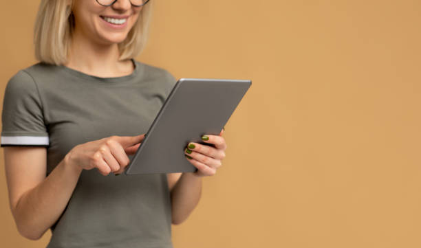 istock Unrecognizable young woman with newest digital tablet standing on beige studio background with empty space 1316590898