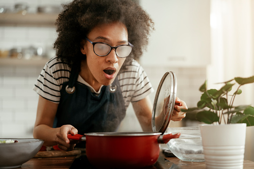 Beautiful woman with curly hair cooking at home. Young woman with steamed glasses cooking pasta