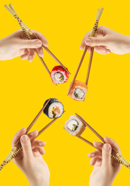 Women's hands hold sushi rolls with sticks. Yellow background. Creative concept