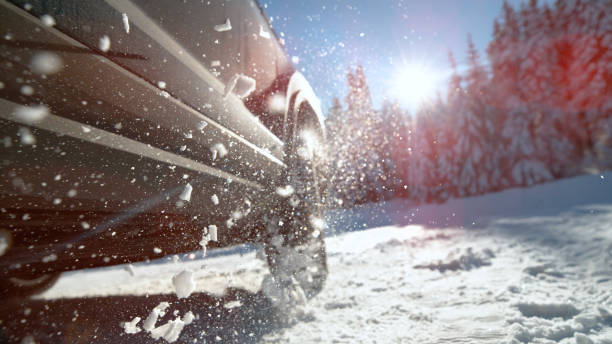LENS FLARE: Metallic blue car throws up chunks of snow while trying to drive.